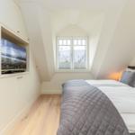 Schlafzimmer mit Dachschrägen, Bett, Fenster und eingebautem Fernseher.