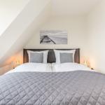 Doppelbett mit grauer Daunendecke unter schrägen Dachfenstern. Wandbild zeigt Strand.