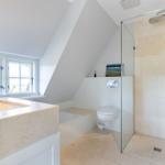 Dusche mit Glaswand, Toilette und Badewanne unter Dachschrägen mit Fenster.