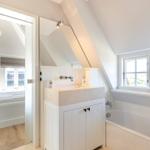 Badezimmer mit Badewanne und Waschbecken. Durchgang in Schlafzimmer mit Bett und Fenster.