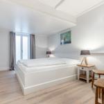 Schlafzimmer mit weißem Bett, Holzstühlen und Fenster. Wandbild und Nachttische.