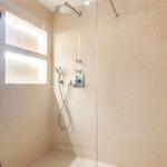 Dusche mit Glaswand, Duschbrause und beleuchteten Wandnischen.