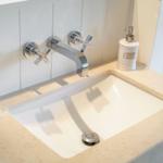 Waschbecken mit Chromarmatur und weißen Flaschen auf Marmorplatte.