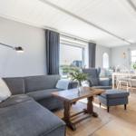 Ein Wohn- und Essbereich mit grauem Sofa, Holztisch und weißen Stühlen.