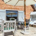 Terrasse mit Tisch, Stühlen, Sonnenschirm und Strandkorb vor Backsteinhaus
