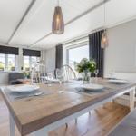 Essbereich mit Holztisch, Stühlen und Fenstern. Helle Wände und Holzboden.