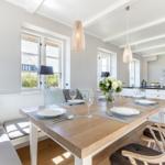 Essbereich mit Holztisch, Stühlen und Fensterblick. Küche im Hintergrund.