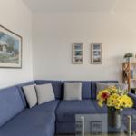 Ein Wohnzimmer mit blauem Sofa, Glas-Tisch und Wandbildern.