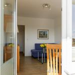 Wohnzimmer mit blauem Sofa, Glasplatte und Holzboden. Fenster zeigt Balkon.