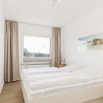 Schlafzimmer mit Doppelbett, Fenster und Holzmöbel.