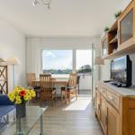 Wohn- und Essbereich mit Balkon, Holzmöbeln und Fernseher.