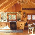 Küche mit Holzmöbeln, Fenstern und Deckenbalken. Ein rosa Kühlschrank und eine Arbeitsplatte sind sichtbar.