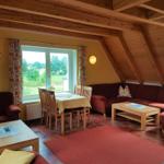 Wohn- und Essbereich mit Holzdecke, Sofa, Tisch und Fensterblick auf Grünland.