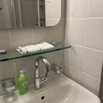 Waschbecken mit Spiegel und Handtuch auf Glasregal.
