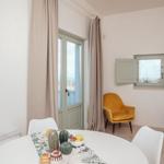 Rundtisch mit Früchten, gelber Sessel, Fenster und Balkontür.