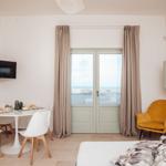 Schlafzimmer mit Essbereich, Bett, gelber Sessel und Fenster mit Meerblick.