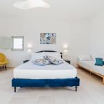 Schlafzimmer mit Bett, Sitzbank und gelber Sessel.