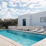 Moderne Villa mit Pool und Liegestühlen im Freien.