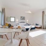 Ein Raum mit Schlafplatz, Esstisch und Fenster. Ein modernes Interieur mit weißen Wänden.