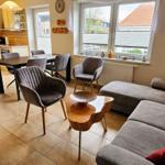 Wohn- und Essbereich mit Sofa, Tisch und Stühlen. Küche mit Arbeitsplatte und Fenster.