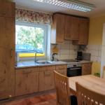 Küche mit Holzschränken, Tisch und Stühlen, Fenster mit Blick nach draußen.