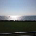 Meer mit Segelboot und zwei Personen im Gras.
