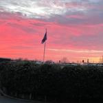 Ein roter Sonnenuntergang mit einer Flagge auf einem Mast hinter Sträuchern.
