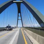 Fahrzeug auf Brücke mit markanter Bogenstruktur und klarem Himmel.