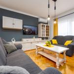 Wohnzimmer mit grauem Sofa, weißem Tisch und TV an grauer Wand.