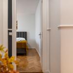 Schlafzimmer mit Bett, gelber Decke und Holzboden. Blick durch Türöffnung.