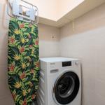 Waschmaschine und Bügelbrett mit tropischem Muster in einem Raum mit Fliesenwänden.
