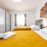 Zwei Betten mit gelben Bezügen und weißen Kissen. Wandbild und Schrank sind sichtbar.