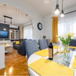 Essbereich mit Tisch und Stühlen. Im Hintergrund Wohnzimmer mit Sofa und Fernseher.