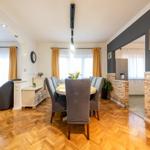 Esszimmer mit Esstisch, Stühlen und Holzboden. Durchgang zu Küche mit Steinwand.