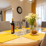 Runde Tisch mit gelben Tischsets, Wein und Blumenarrangement.