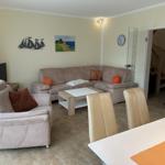 Wohn- und Essbereich mit Sofa, Sessel und Tisch. Wanddekoration und Treppe sichtbar.