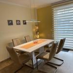 Essbereich mit weißem Tisch, sechs braunen Stühlen und Fenster mit Jalousien.