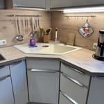 Küche mit Arbeitsfläche, Spüle und hängenden Küchenutensilien.