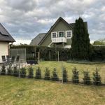 Haus mit Garten, Terrasse und Holzveranda. Umzäunt mit Metallzaun und Beerensträuchern.
