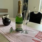 Auf dem Tisch steht eine Flasche Sekt und zwei Gläser auf einem Tischläufer.
