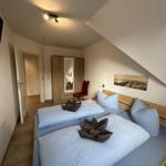 Doppelbett mit blauen Bettwäsche und Holzrahmen. Wandbild, Kleiderschrank und roter Stuhl.