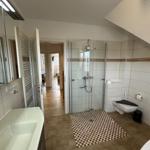 Badezimmer mit Dusche, WC und Waschbecken. Fliesenboden und Spiegel.