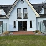 Moderne Villa mit Terrasse und grünem Garten. Eingangstür und Fenster sind schwarz.