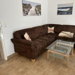 Wohnzimmer mit braunem Sofa, Glas-Tisch und Wandbildern