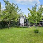 Garden with glasshouse, grill shed, and trees under blue sky.