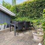 Terrace with table and chairs in front of gray house with hedge.