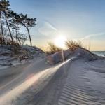 Weg durch Sanddünen zum Meer bei Sonnenuntergang mit Bäumen am Horizont