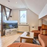 Wohnzimmer mit Sofa, Fernseher und Holzboden. Fenster mit Blick auf Haus.