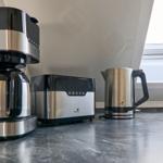 Küchenzeile mit Kaffeemaschine, Toaster und Wasserkocher auf Arbeitsfläche.
