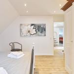 Schlafzimmer mit Bett, Wandbild und Blick in Wohnbereich.